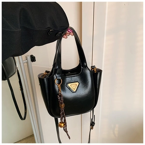 Detail of black leather bucket bag featuring a gold logo and woven bell charm accessory