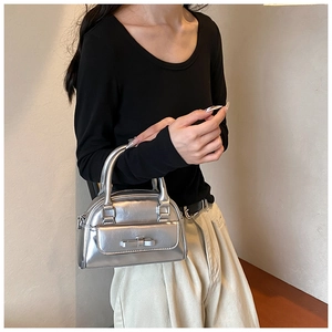 Detail of silver metallic shell bag featuring a chic bow pocket and round top handles