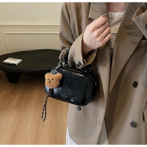 Détail du sac bowling noir brillant avec finitions argentées et charm ours en peluche