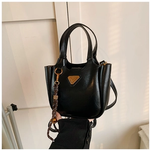 Close-up of black glossy leather bucket bag with gold triangle plate and woven charm