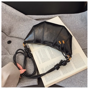 Detail of black glossy leather croissant bag with knotted strap on a wool coat