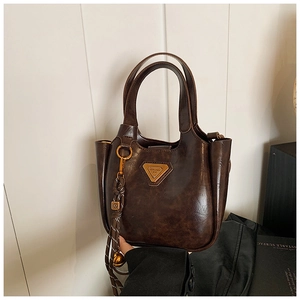 Macro detail of brown leather bucket bag with golden triangle plaque and metal charms