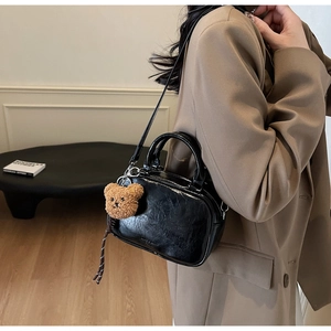 Détail du sac bowling en cuir noir brillant avec texture vintage et breloque ours marron