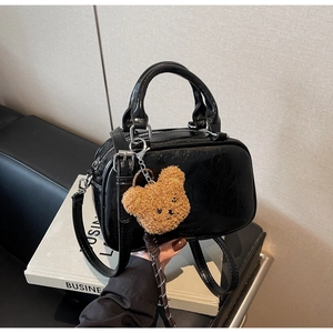 Détail d'un sac bowling en cuir verni noir brillant avec un pendentif ours en peluche