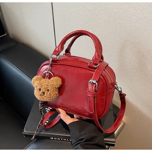 Détail d'un sac à main rouge vintage verni avec pendentif ours sur fond épuré