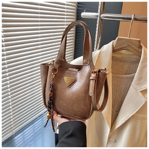 Detail of vintage brown tote bag with gold triangle plate and woven bell charm