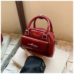 Close-up of deep red glossy Boston bag with bow decoration and silver zipper detail