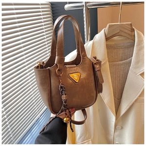 Detail of a brown bucket bag featuring a woven knot charm and golden bell accessory