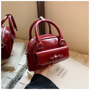 Detail of a dark red patent leather Boston bag featuring a bow and smooth glossy finish