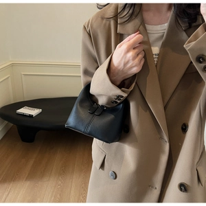 Detail of a black minimalist trapezoidal handbag with dual zippers and smooth matte leather