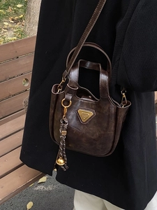 Vintage dark brown bucket bag in trapezoid shape with golden metal plaque and knot charm
