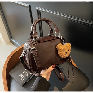 Détail d'un sac Boston vintage marron foncé avec un charm ours et une bandoulière fine