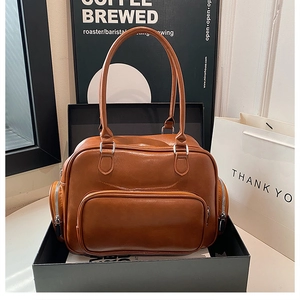 Detailed view of a brown leather handbag with side zippers in a gift box packaging