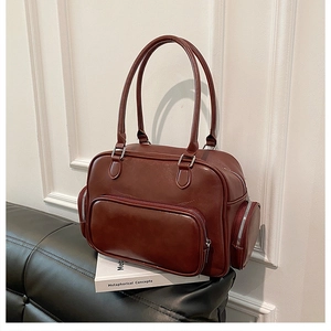 Detail of burgundy faux leather handbag with side zip pockets on a vintage studio sofa