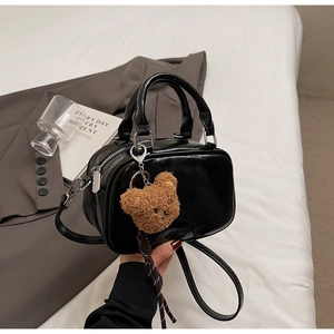 Détail d'un sac bowling en cuir noir brillant avec breloque ours sur un blazer gris