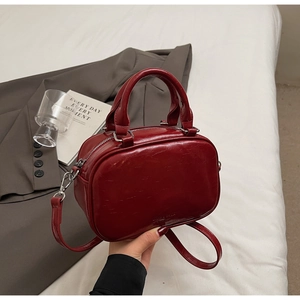 Détail d'un sac en cuir verni rouge foncé avec fermetures éclair argentées et anses