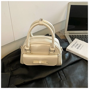 Detailed view of cream Boston bag with bow accent on a sleek black leather surface