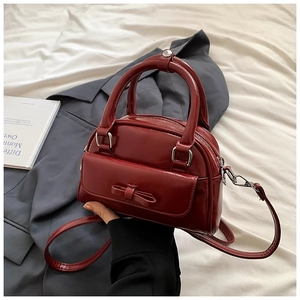 Close-up of a glossy red Boston bag with bow detail and silver metal hardware accents