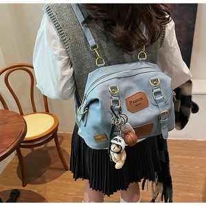 Detail of light blue denim backpack with brown leather patches and cute plush bear charm