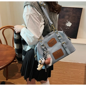 Detail of grey-blue Boston bag featuring a bear charm and brown brand logo patches