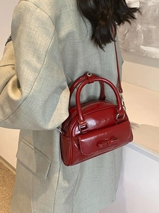 Glossy red Boston bag with bow detail and silver hardware shown on a model
