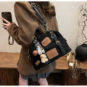 Detail of a large black canvas tote with leather patches and a cute plush bear pendant