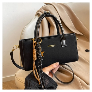 Detailed view of black textured shoulder bag with gold hardware and star pendant accessory