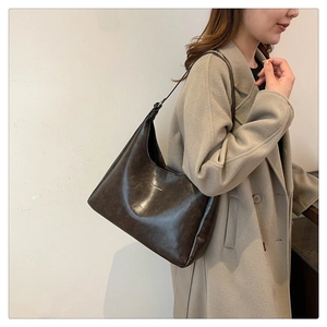 Detail of vintage brown leather hobo shoulder bag shown on a model in a beige coat