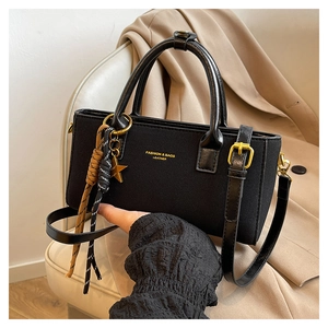 Detail of black leather handbag with gold star charm and braided tassel accents