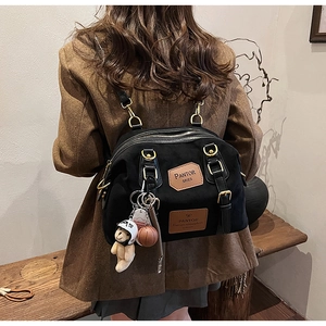 Detail of black canvas backpack with brown leather trim and teddy bear charm accessory