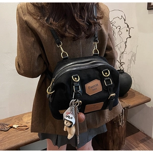 Close-up of black denim backpack with leather straps and bear charm shown on a model