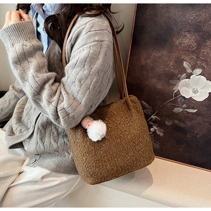 Détail du sac cabas en peluche marron chaud avec pompon et bandoulières dans un décor doux