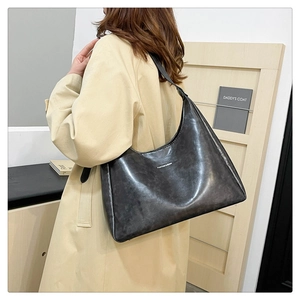 Detail of dark grey faux leather shoulder bag texture on a model wearing a trench coat