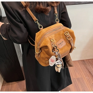 Close-up of brown suede backpack with plush lamb charm and leather brand patch