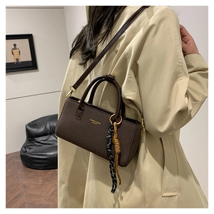 Detail view of coffee brown faux leather handbag with side rope ornament on trench coat