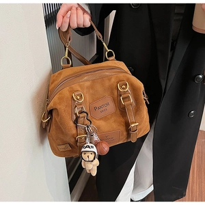 Detail view of brown faux suede Boston bag featuring embossed logos and bear charm