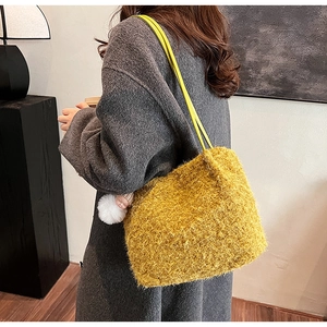 Sac seau en peluche jaune avec texture douce et breloque poupée portés à l'épaule de dame