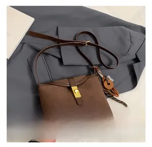 Detail of brown suede bucket bag featuring a golden twist lock and fringe tassel accent