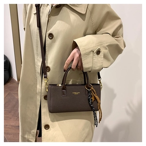 Detail of a dark brown crossbody bag with gold lettering and star-shaped charm