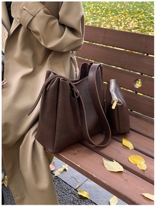 Detail of dark brown leather tote bag and small pouch on a park bench with autumn leaves