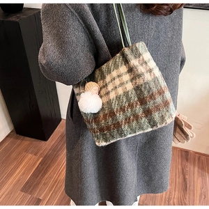 Détail du sac cabas en laine à carreaux verts avec un pendentif pompon blanc élégant