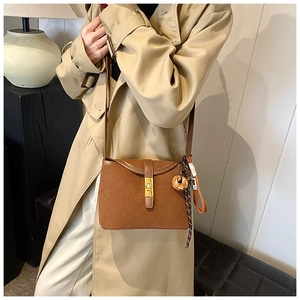 Brown frosted leather crossbody bucket bag with gold ring and woven tassel on a trench coat