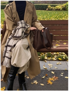 Close-up of a large dark brown leather tote bag on a park bench in autumn setting