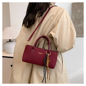 Detail of dark red crossbody bag with star charm pendant and woven rope decoration