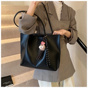 Detail of a black large-capacity leather tote bag with a small plush lamb charm pendant