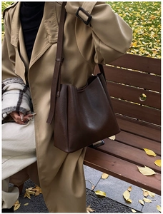 Detail view of a vintage dark brown leather bucket bag on a model in autumn scenery