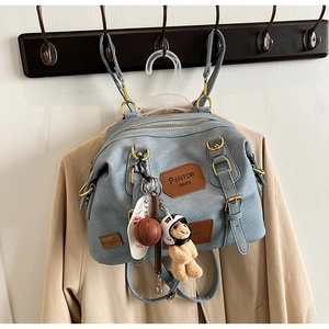 Detail of light blue denim-style backpack with teddy bear charm and brown leather patches
