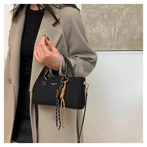 Detail of a black leather handbag with gold hardware and woven tassel on beige coat