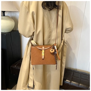 Close-up of brown suede crossbody bag featuring a golden metal buckle and decorative strap