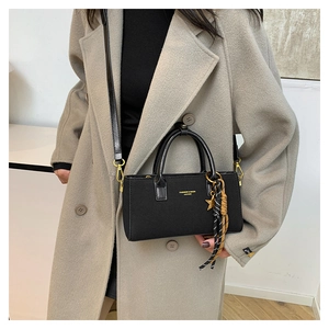 Detail of black leather handbag with gold hardware and star scarf charm on model